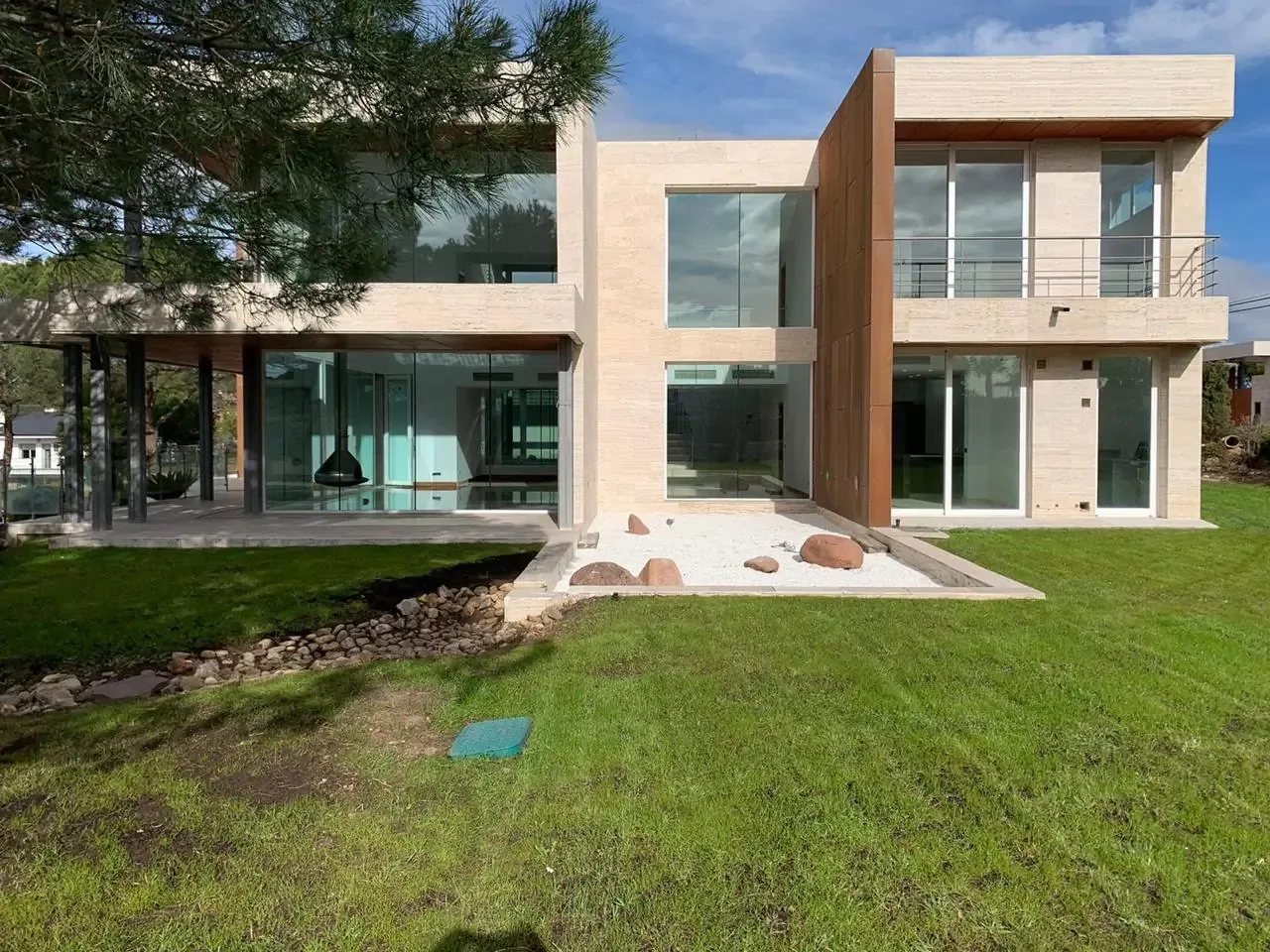 Fachada de la vivienda de Boadilla del Monte, con dos cuerpos, plano de piedra en el acceso, revoco claro y césped en primer plano.