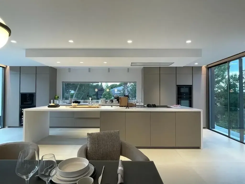 Cocina con isla central, taburetes y frentes sin tiradores abiertos al comedor.