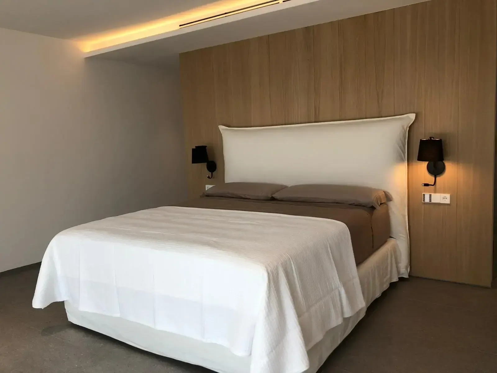 Dormitorio con pared revestida de madera, apliques de pared y textiles en blanco.
