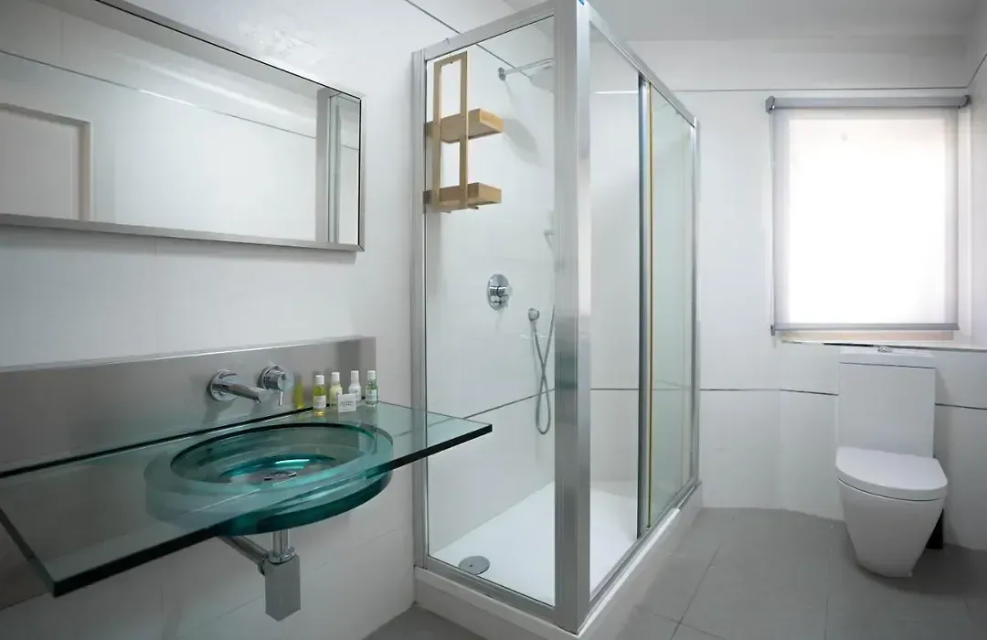 Baño con lavabo de cristal, espejo horizontal y ducha con mampara.