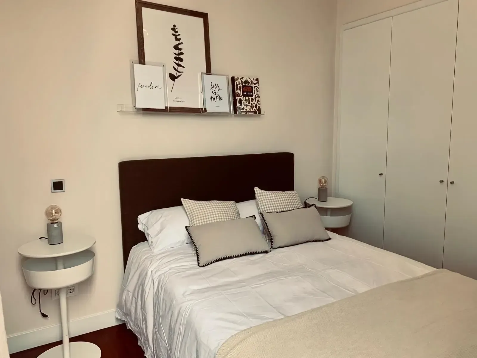 Dormitorio con cabecero de madera oscura, mesillas redondas y láminas enmarcadas sobre la cama.