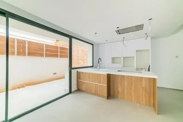 Cocina recién entregada, con muebles blancos, frente de madera y carpintería de ventana en verde.