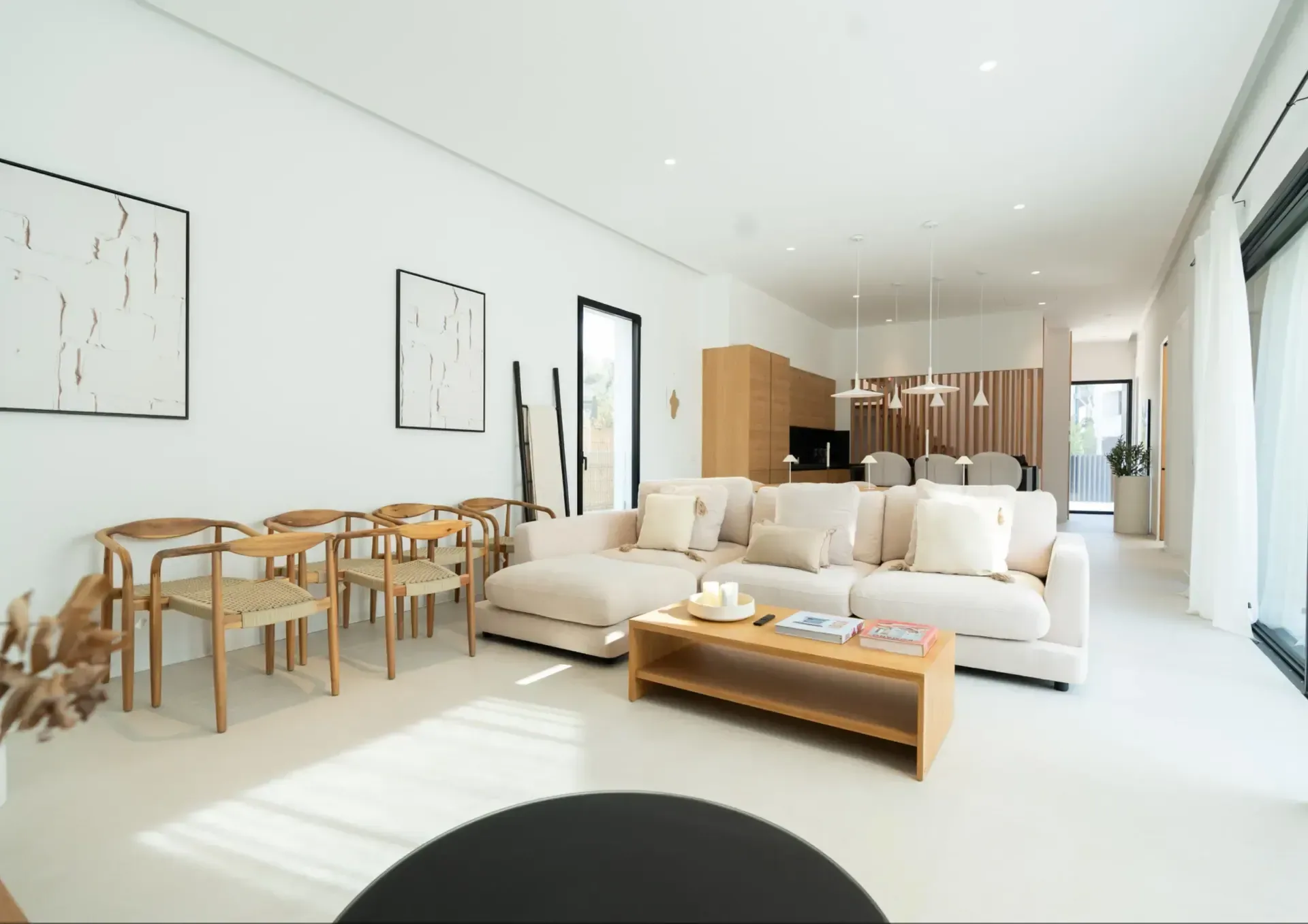 Salón comedor diáfano con sofá claro, mesa de madera y carpintería de suelo a techo abierta a la terraza.