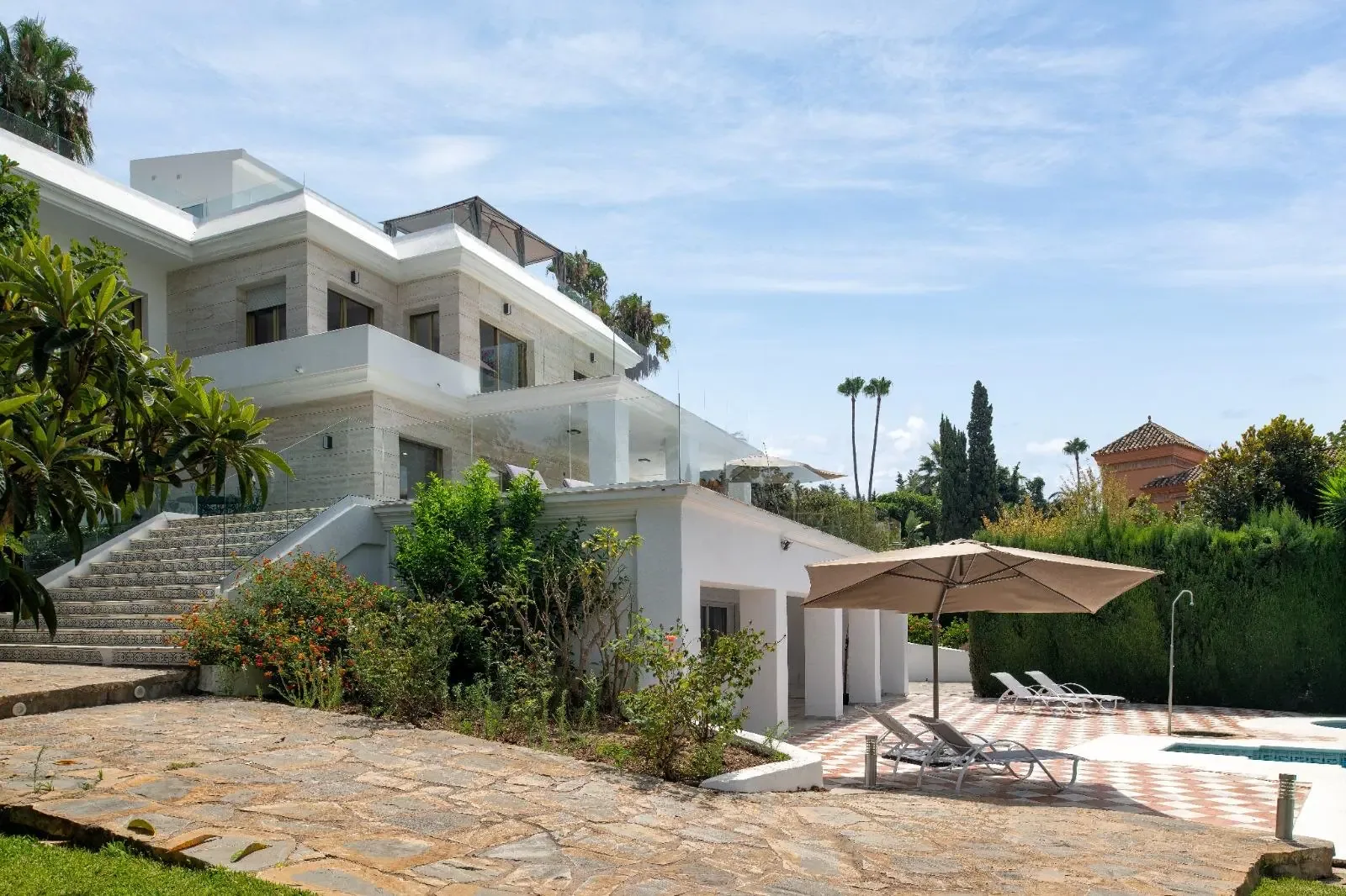 Cuerpo lateral de la villa con escalera exterior de acceso y pavimento de piedra clara.