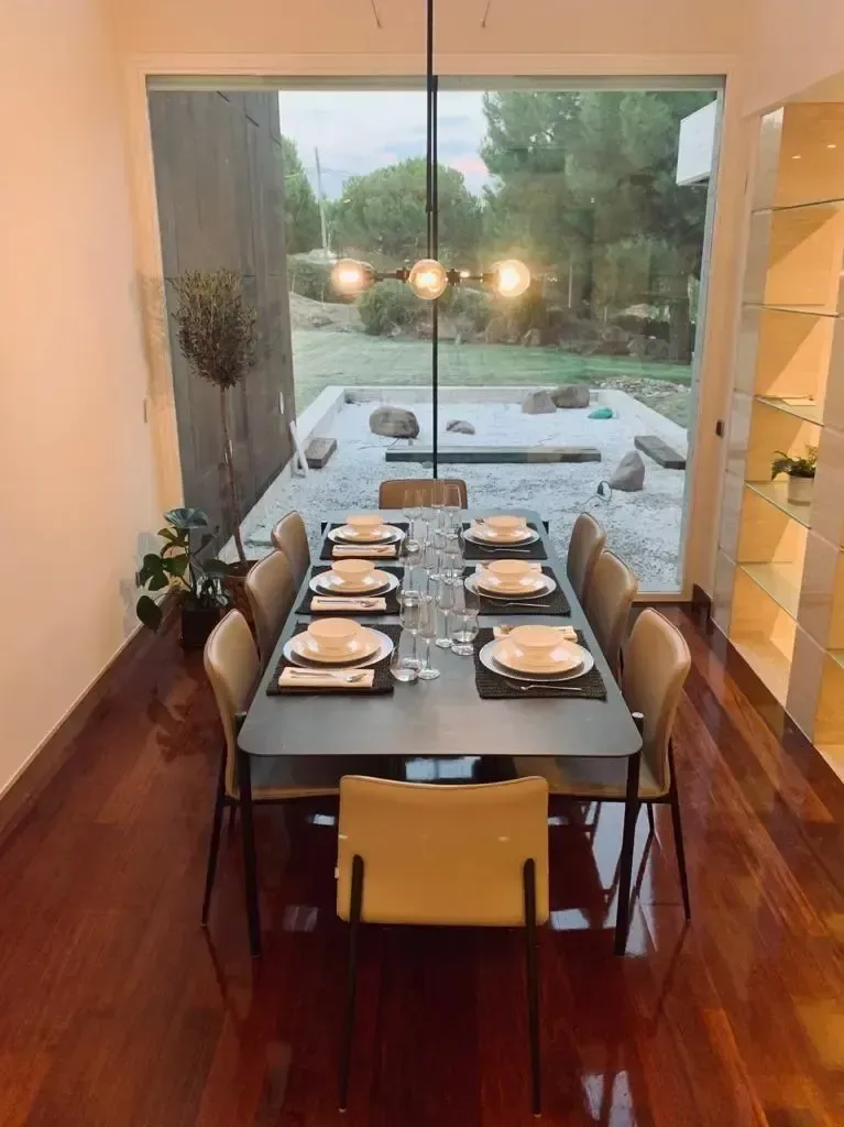 Comedor con mesa larga de madera, lámpara suspendida y servicio dispuesto para varios comensales.