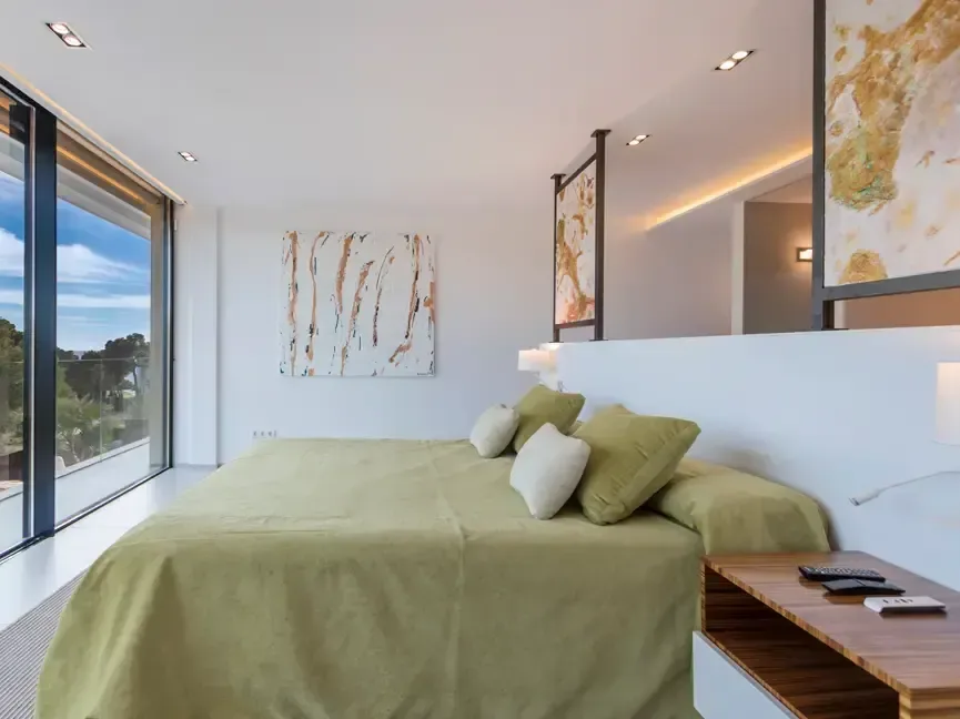 Dormitorio con ropa de cama en tono oliva, cabecero bajo y ventanal horizontal hacia el exterior.