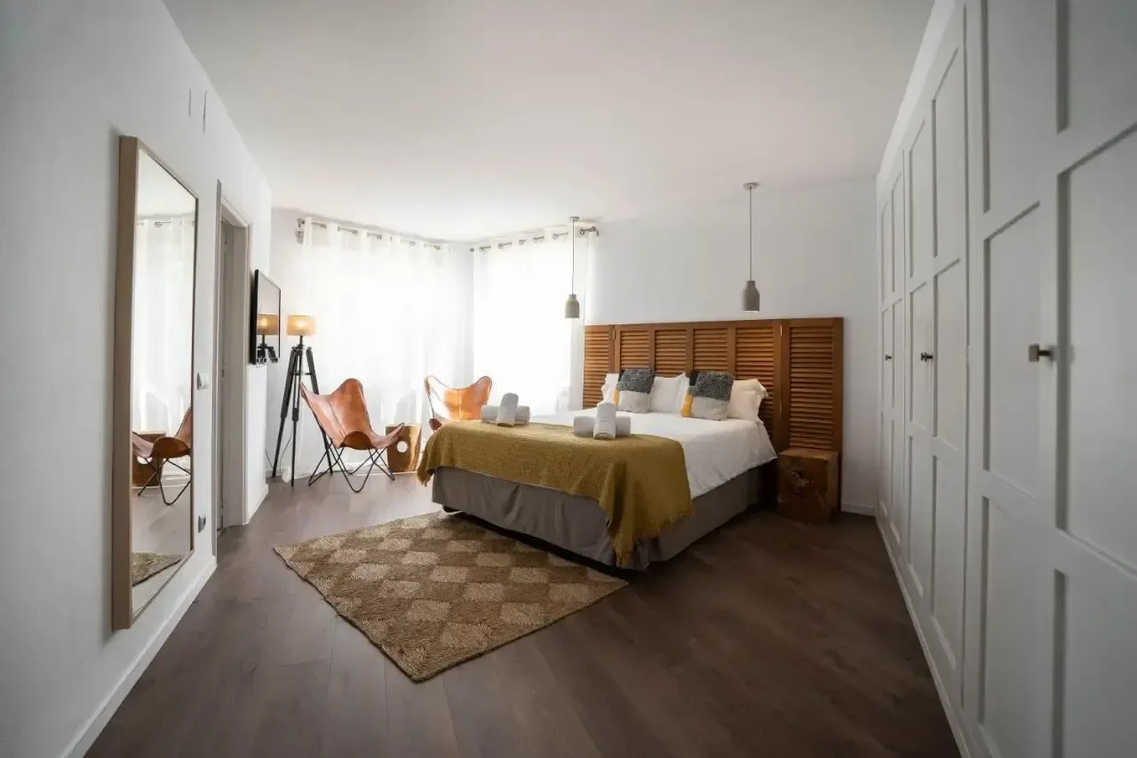 Dormitorio con cabecero de madera, frente de armarios blanco y suelo de tarima oscura.