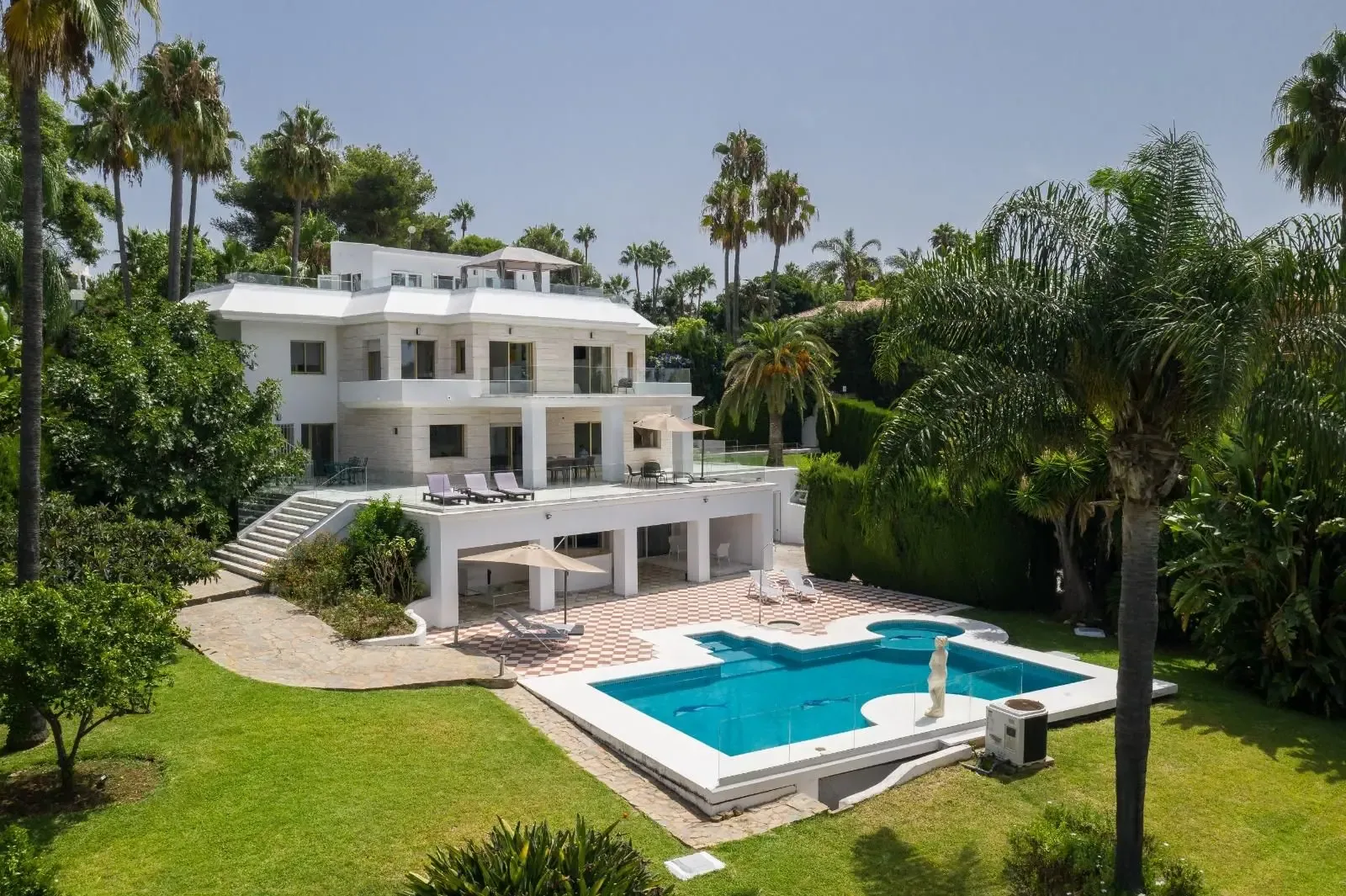 Fachada sur de la villa con la piscina en primer plano, tumbonas y vegetación subtropical.
