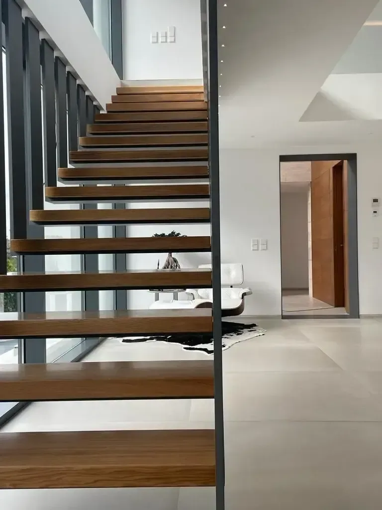 Escalera volada con peldaños de roble macizo, zanca de acero negro y barandilla de pletinas verticales.