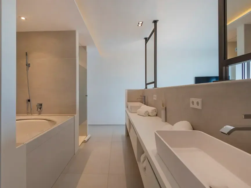 Baño revestido en piedra caliza, con bañera integrada en la obra y encimera continua de doble seno.