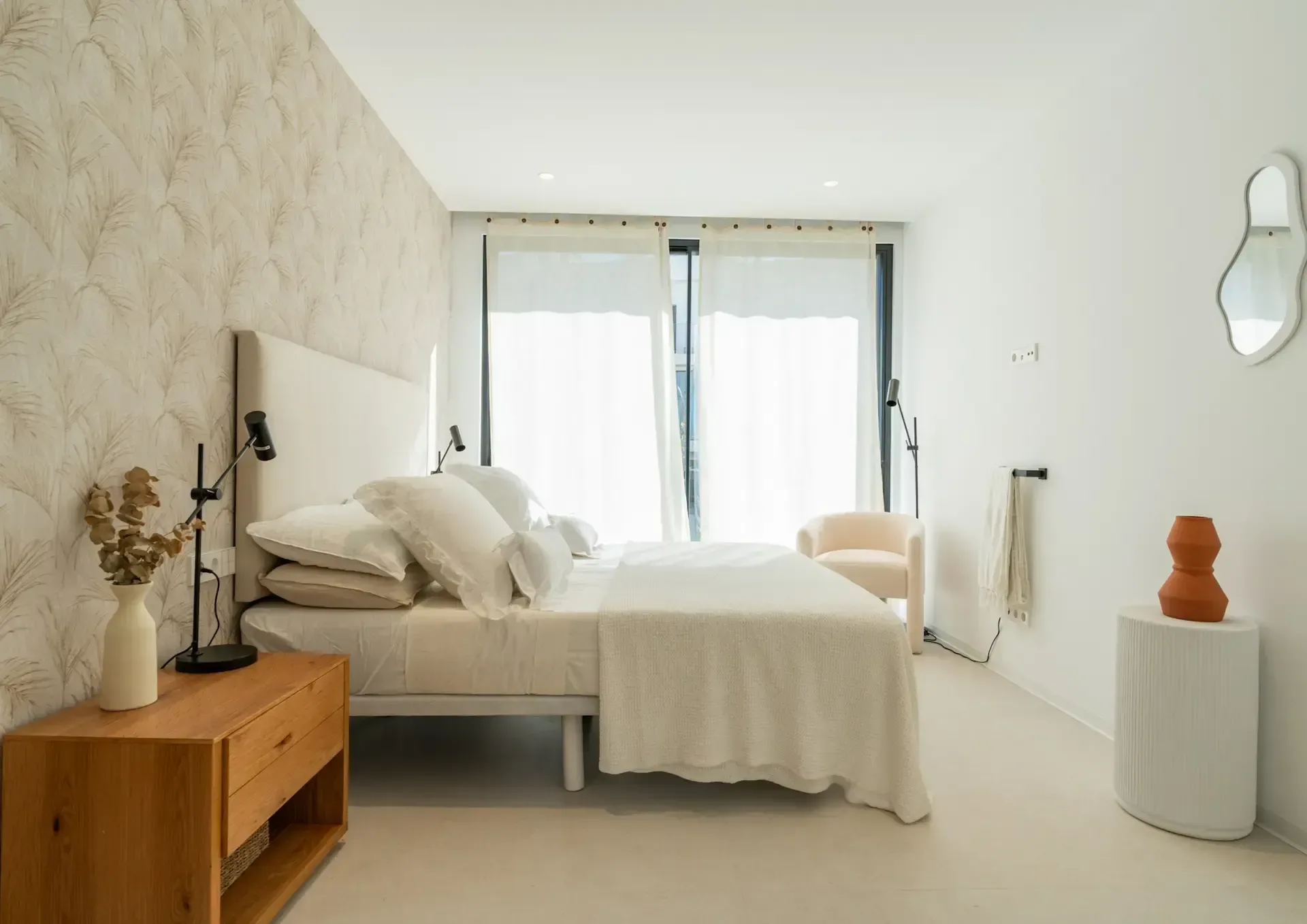 Dormitorio con cabecero tapizado, mesilla de madera maciza y pared texturizada en tono cal.