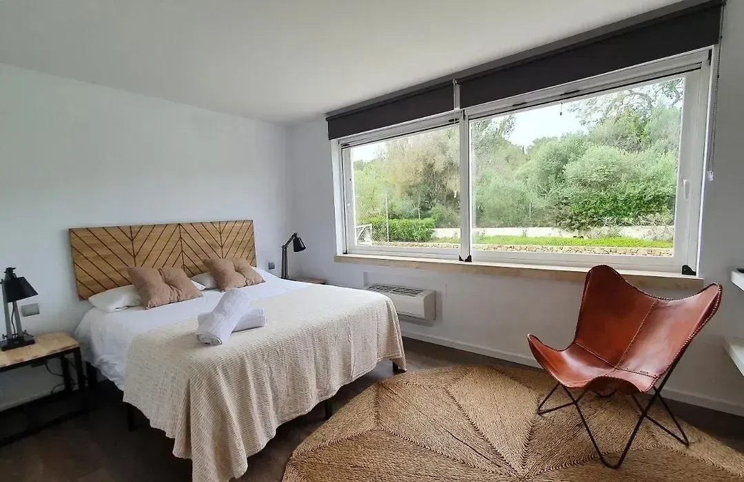 Dormitorio con cabecero tejido, butaca de color teja y ventana hacia la vegetación.