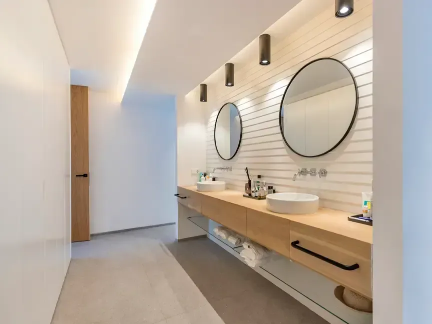 Baño con dos espejos circulares, mueble de madera suspendido y pared de lamas verticales.