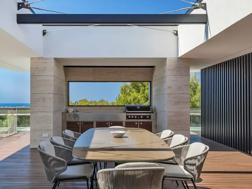 Zona de comedor bajo techo de madera, abierta al exterior por un frente acristalado con vistas al campo.