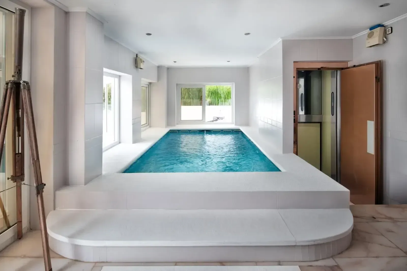 Sala de la piscina interior, con paramentos blancos y hueco de luz natural.