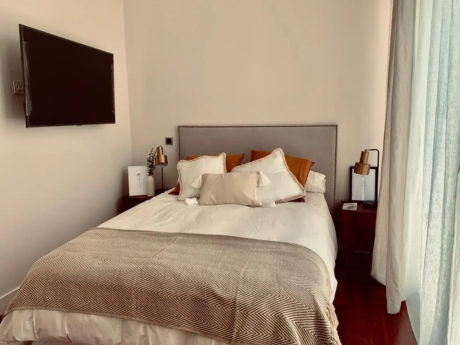 Dormitorio con televisor de pared, cortinas claras y armario integrado.
