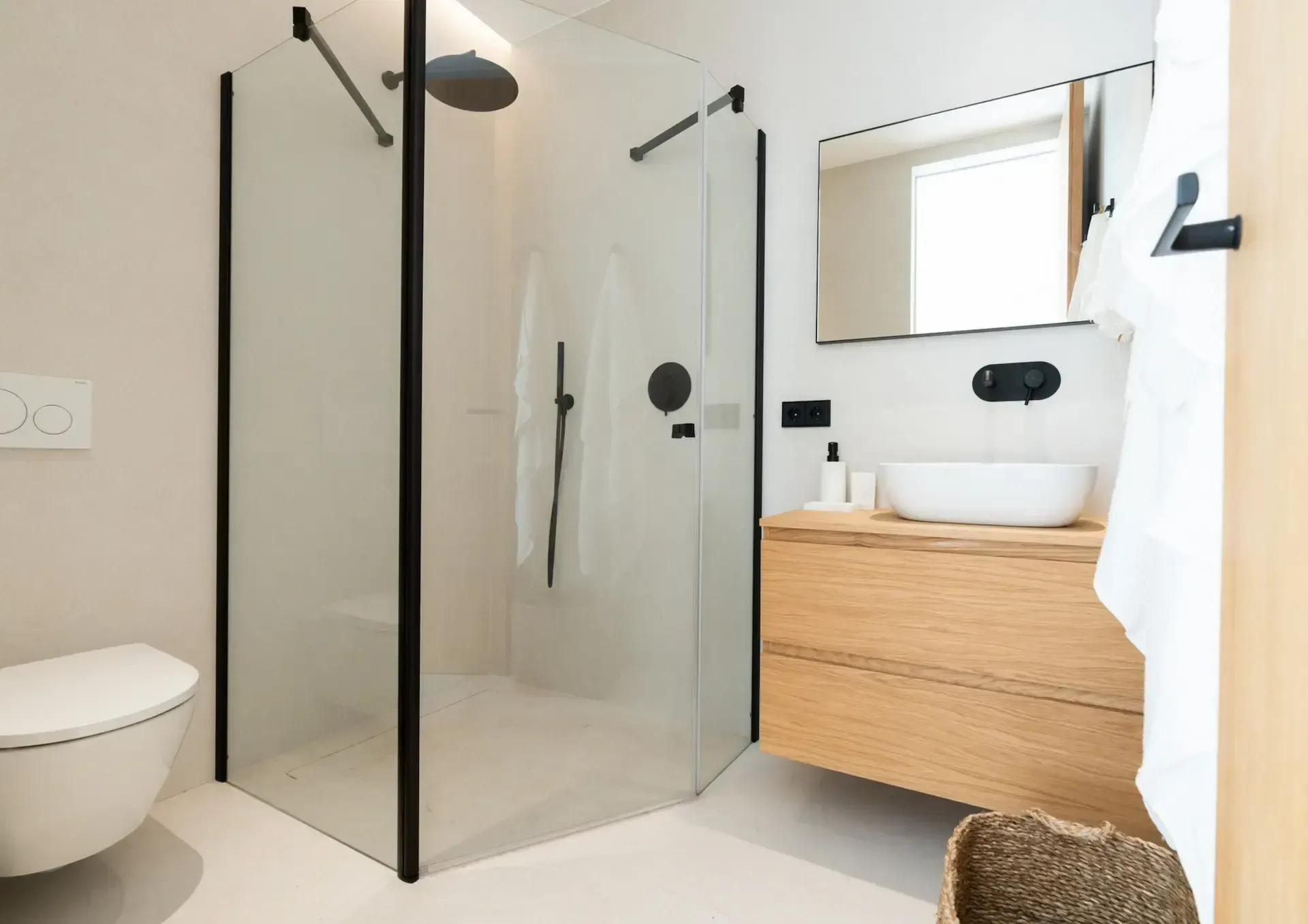 Baño con ducha a ras de suelo, mampara de perfilería negra y mueble de roble con encimera blanca.