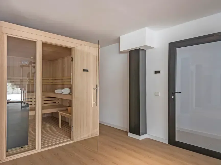 Sauna con frente acristalado y revestimiento interior de madera, junto al paso de servicio.