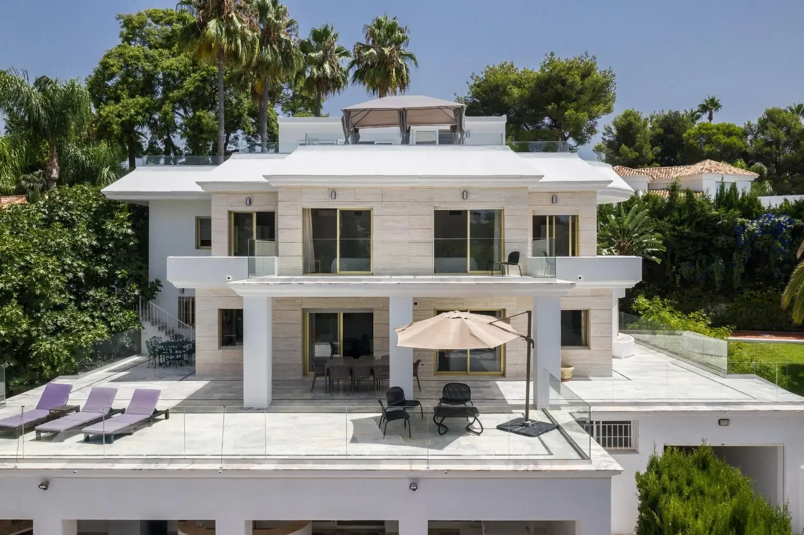 Fachada principal de la villa de Marbella, con terrazas superpuestas y barandillas blancas.